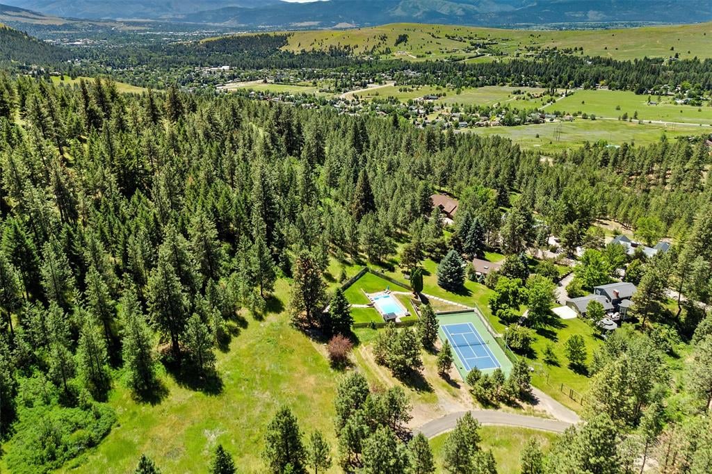 Aerial view of wooded homes with a swimming pool and tennis courts in a mountain valley.