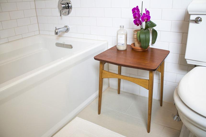Bathroom with a white bathtub, wooden side table, bath salts, and purple orchid.