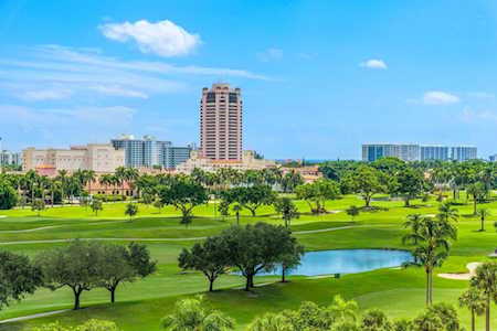 East Boca golf course with a pond and palm trees, with mid-rise buildings in the distance.