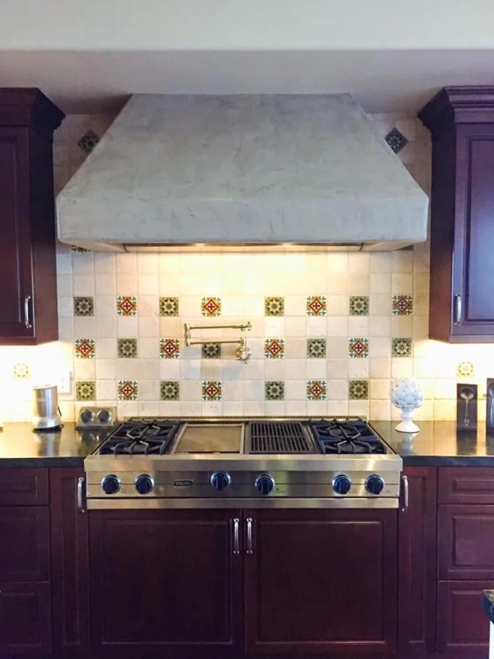Kitchen with a stainless-steel range, broad white hood, and colorful patterned tile backsplash.