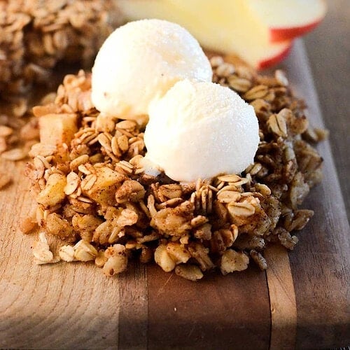 Apple cinnamon granola with apple pieces and two white scoops on a wooden board.