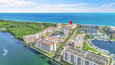 Coastal condominium development between the ocean and waterways, with a red arrow marking a beachfront building.