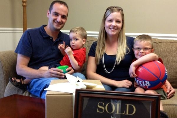 Brian and Danielle with their two young children beside a framed SOLD sign.