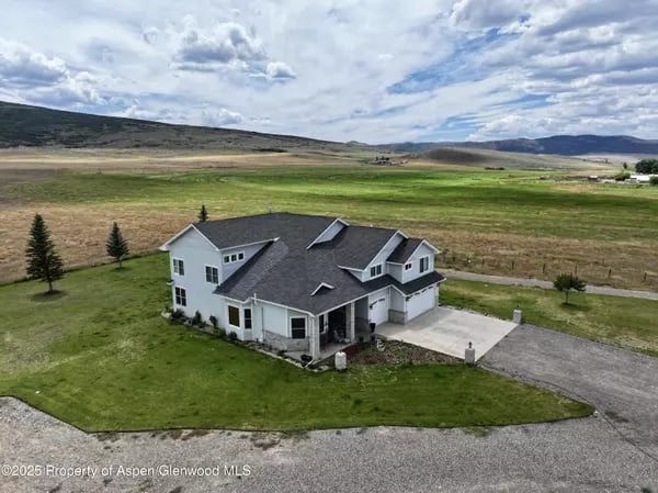 Aerial view of a white two-story home with a dark roof on a broad rural lot.