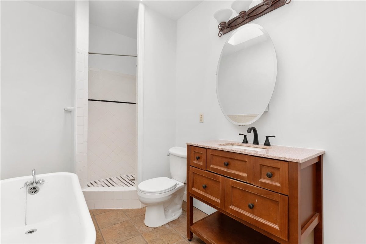 Bathroom with a wood vanity, oval mirror, bathtub, and tiled walk-in shower.