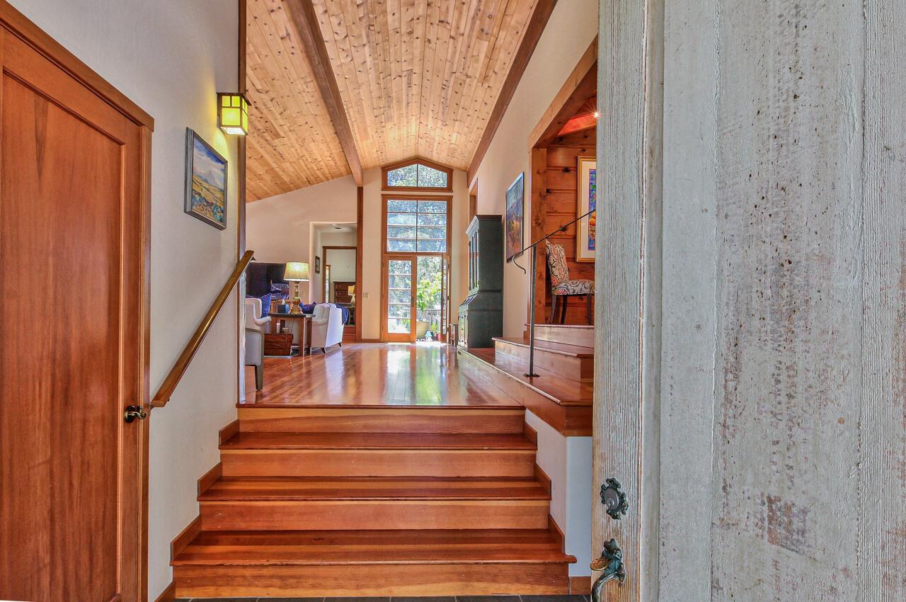 Entryway with wooden stairs leading to a vaulted living area with tall windows.