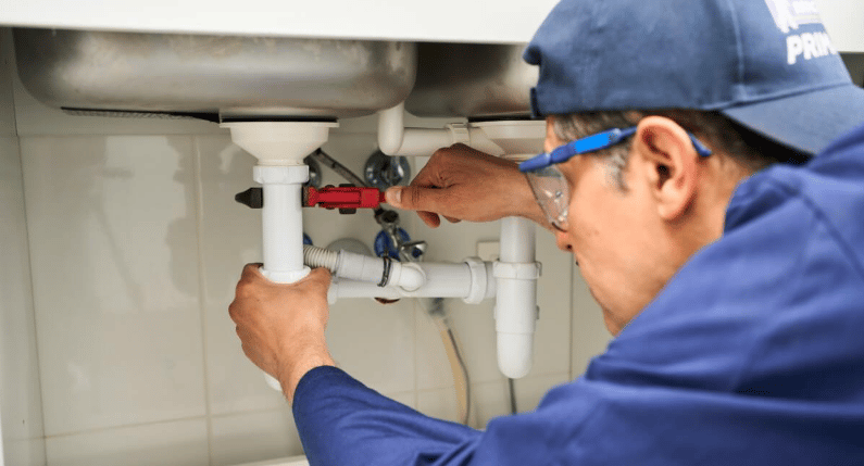 A plumber adjusts white drain pipes beneath a sink.
