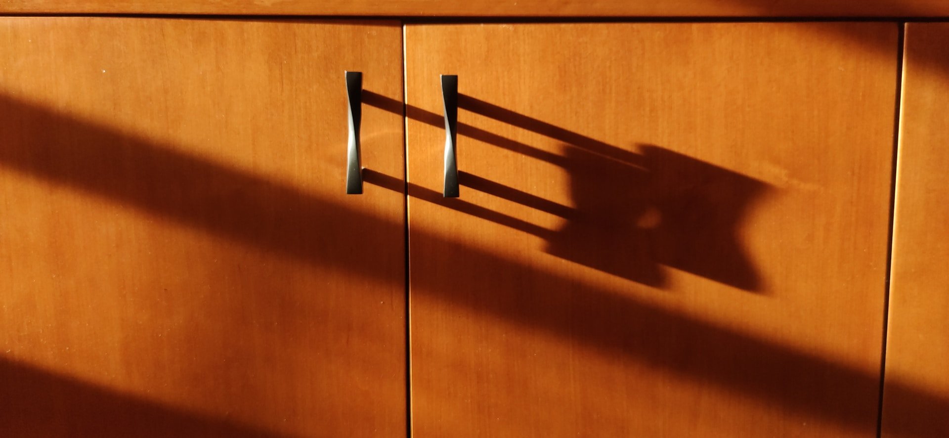 Wooden cabinet doors with dark handles and long shadows from sunlight.