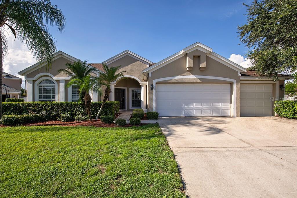 Single-story stucco home with palm trees, a green lawn, and an attached two-car garage.
