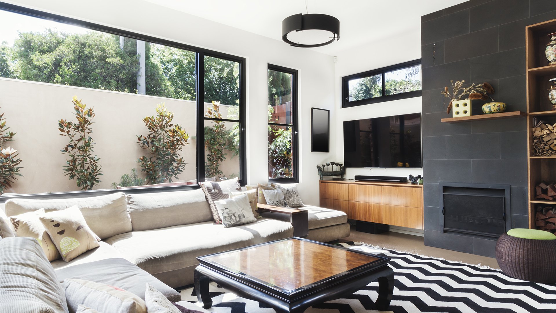Modern living room with a cream sectional, large windows, and a dark tiled fireplace.