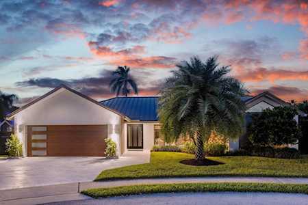 Modern single-story home with a blue metal roof and a palm tree in the front yard at dusk.