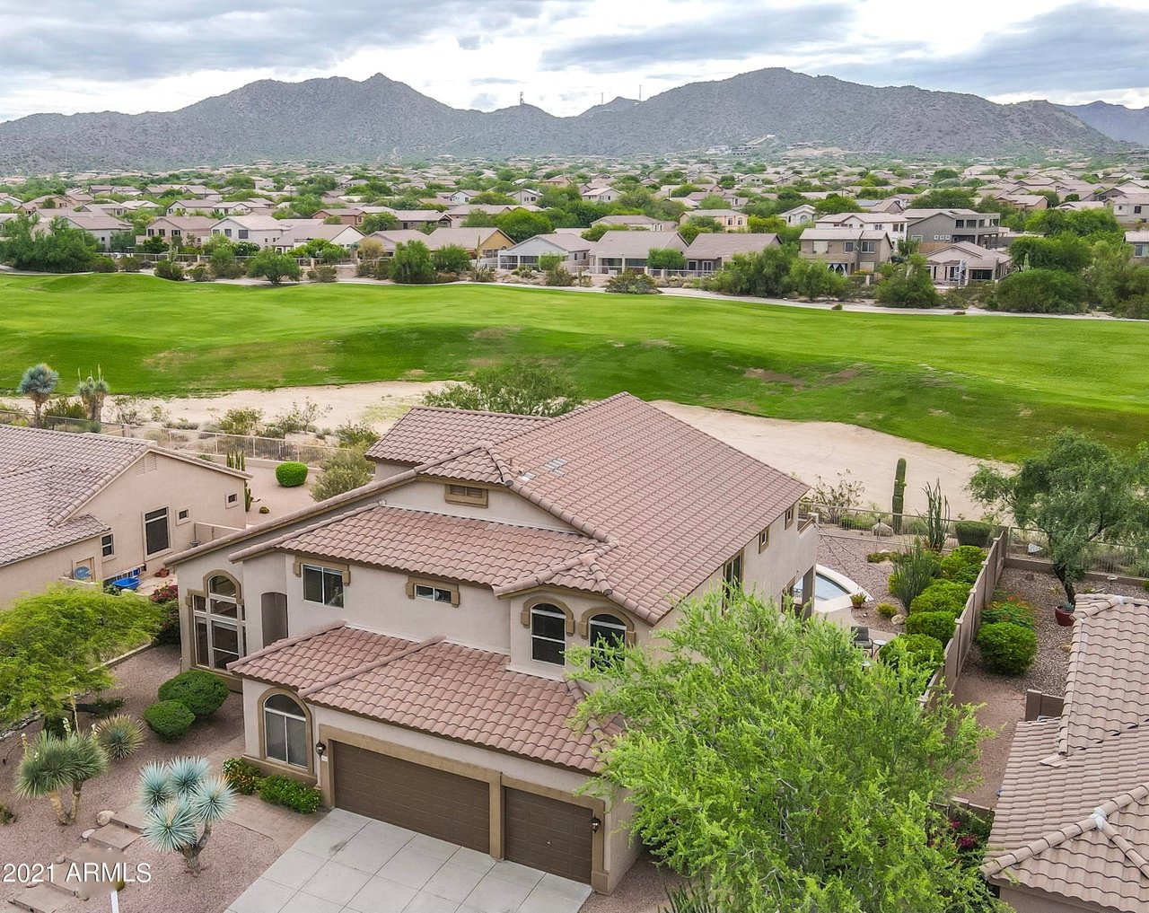 Aerial view of a stucco home beside a golf course, with desert mountains beyond.