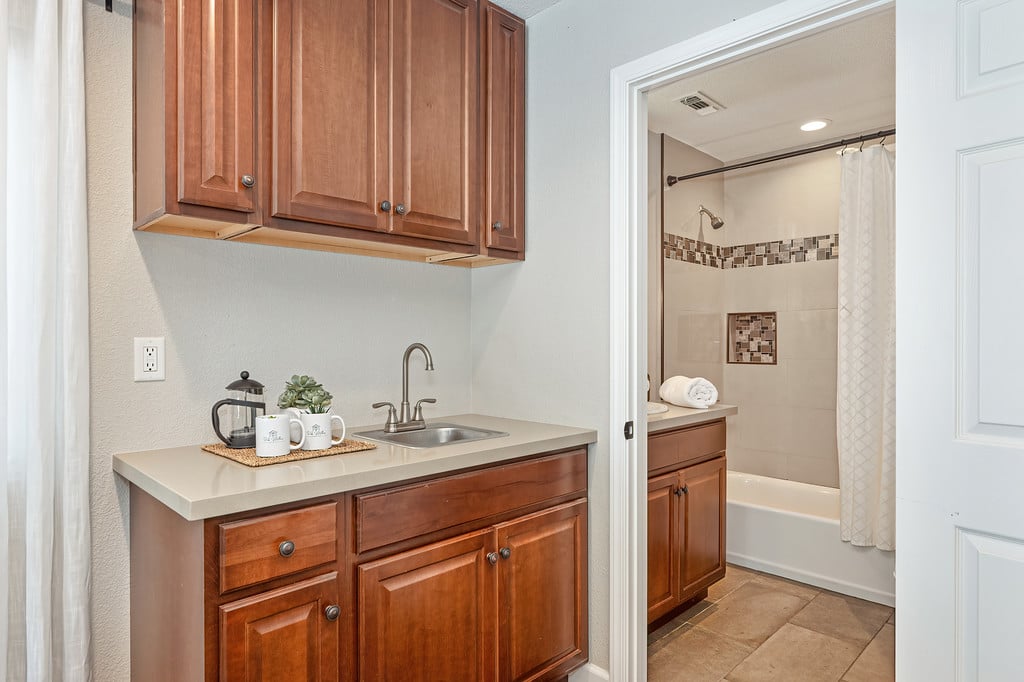 Bathroom vanity with wood cabinetry beside a tiled tub and shower.