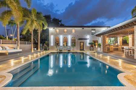 Modern home with an illuminated pool, palm trees, and a covered outdoor entertaining area at night.