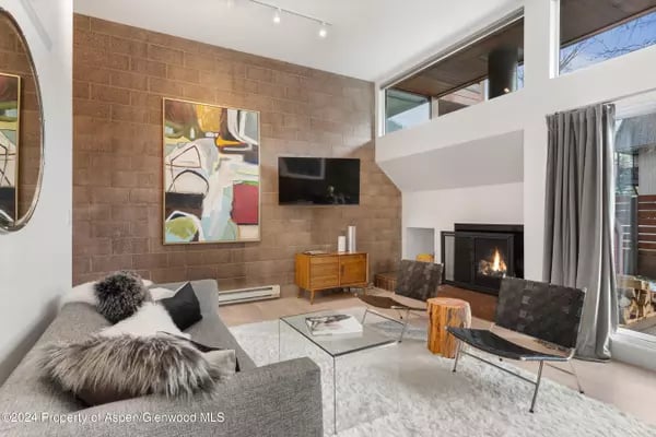 Furnished living room with a tall brick wall, abstract artwork, and a fireplace.