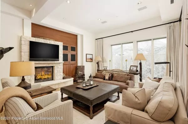 Living room with a stone fireplace, cream sofas, and windows overlooking snowy mountains.