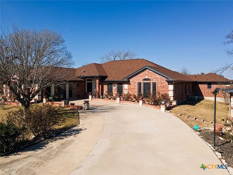 Single-story brick home with a broad curved driveway and leafless trees.