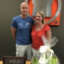 Mike and Shelly stand beside a SOLD plaque and a wrapped bouquet.