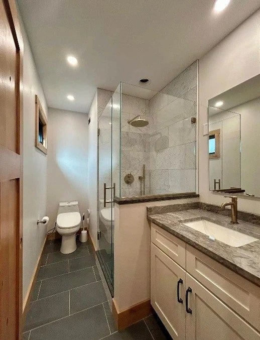 Renovated bathroom with a glass shower, gray tile floor, and white vanity with stone countertop.
