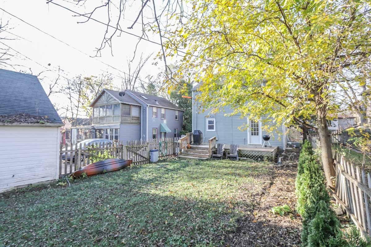 Blue-gray two-story house behind a fenced backyard, with a raised deck and autumn trees.