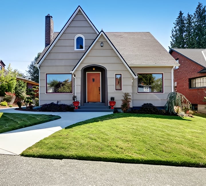 Small gray house with steep gables, a wood front door, and a green front lawn.
