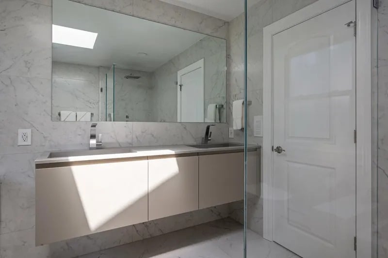 Modern bathroom with a floating double-sink vanity, marble surfaces, and a glass shower partition.