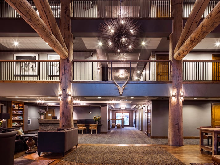 Two-story lodge great room with massive timber beams, an antler wall mount, and a spiky chandelier.