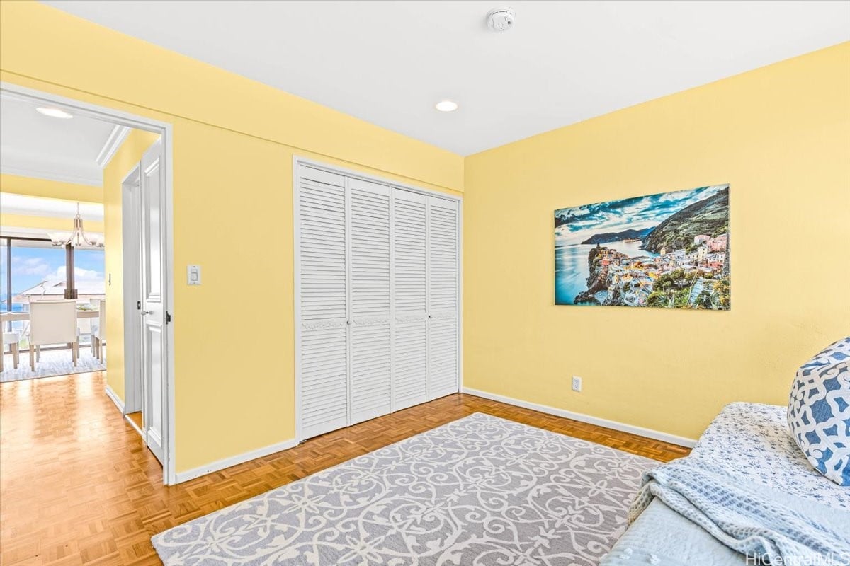 Yellow bedroom with white louvered closet doors, parquet flooring, and a patterned rug.