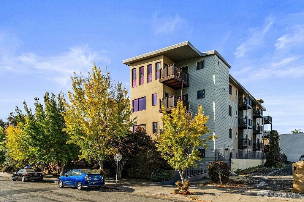 Modern apartment building with multiple balconies, autumn trees, and parked cars along the street.