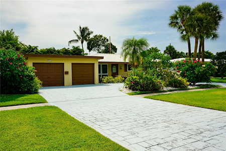 Single-story home with two garage doors, a broad paved driveway, and tropical landscaping.