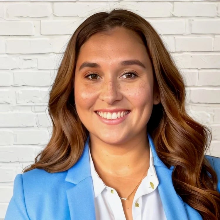 Ashley Connell smiling in a blue blazer against a white brick wall.