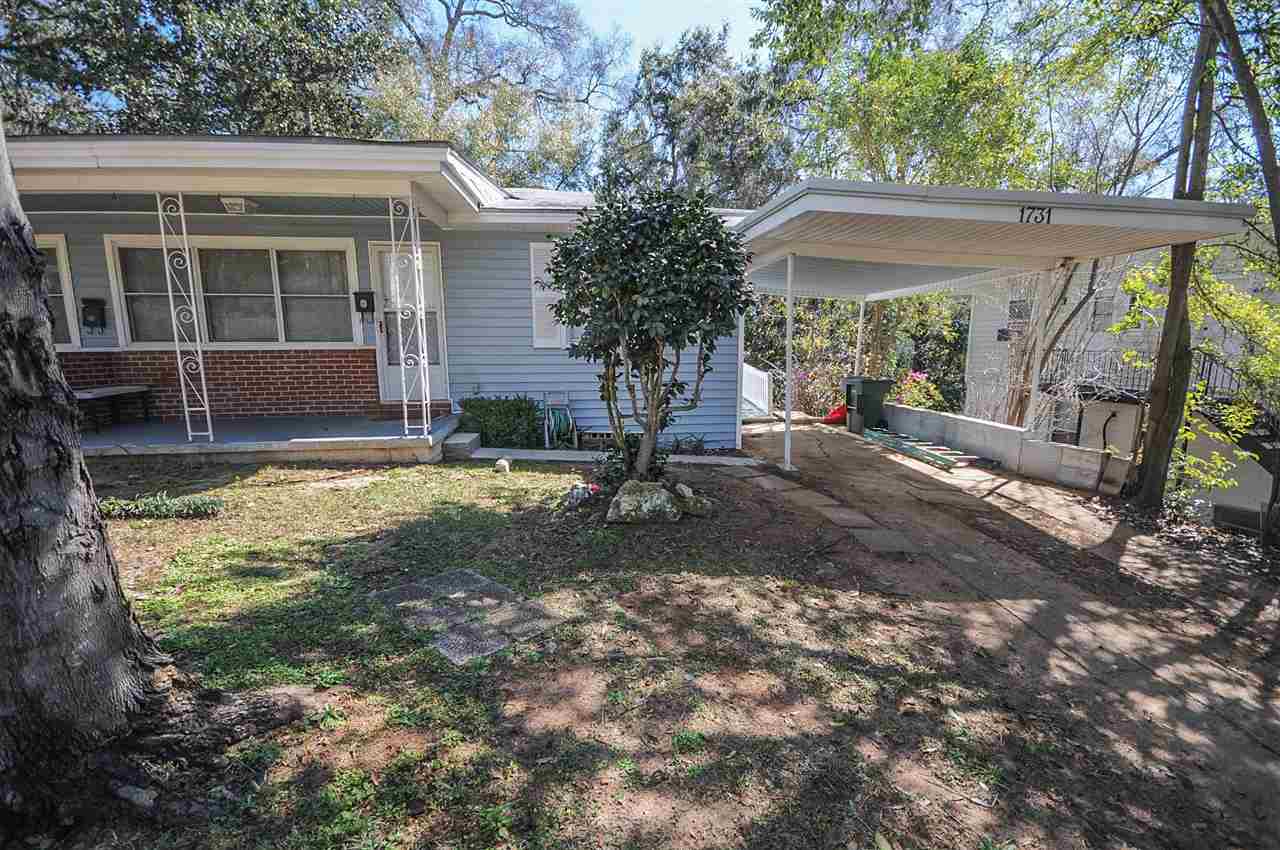 A small house featuring a covered porch, surrounded by lush trees, creating a serene and inviting atmosphere.