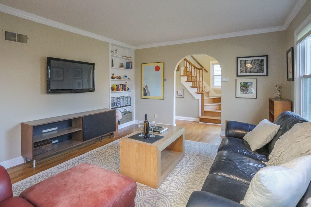 Living room with a leather sofa, built-in shelves, and an arched opening to a wooden staircase.