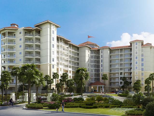 Multi-story condominium with glass balconies, palm trees, and landscaped gardens.