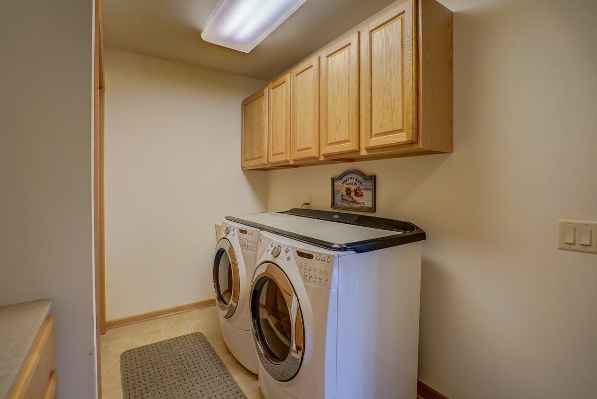 Laundry room with front-loading washer and dryer beneath light wood cabinets.