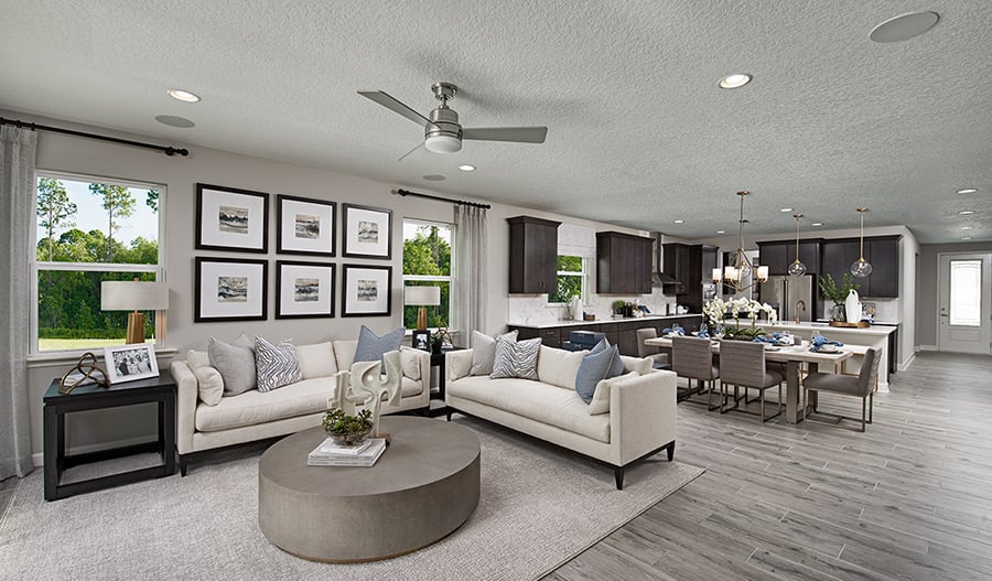 Staged living room with open kitchen and dining area, large windows, and round coffee table.