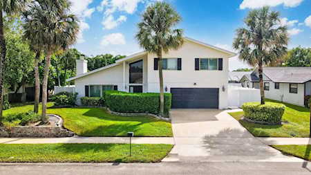 Modern two-story home with a dark garage, palm trees, and a manicured front lawn.