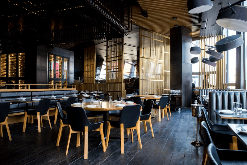 Restaurant dining room with dark chairs, wood slat partitions, and large windows.