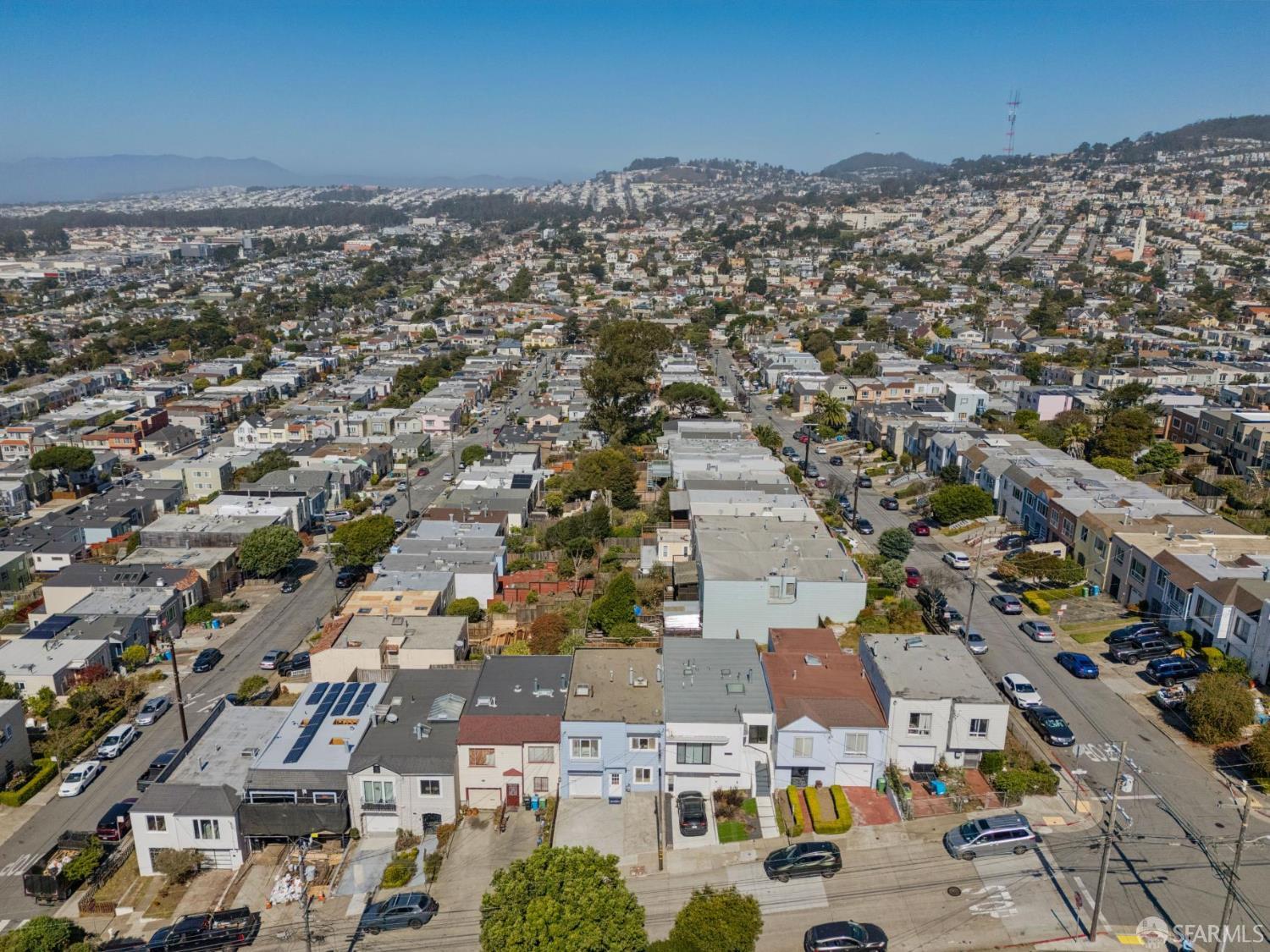 Aerial view over a dense neighborhood of homes, with San Francisco’s hills in the distance.