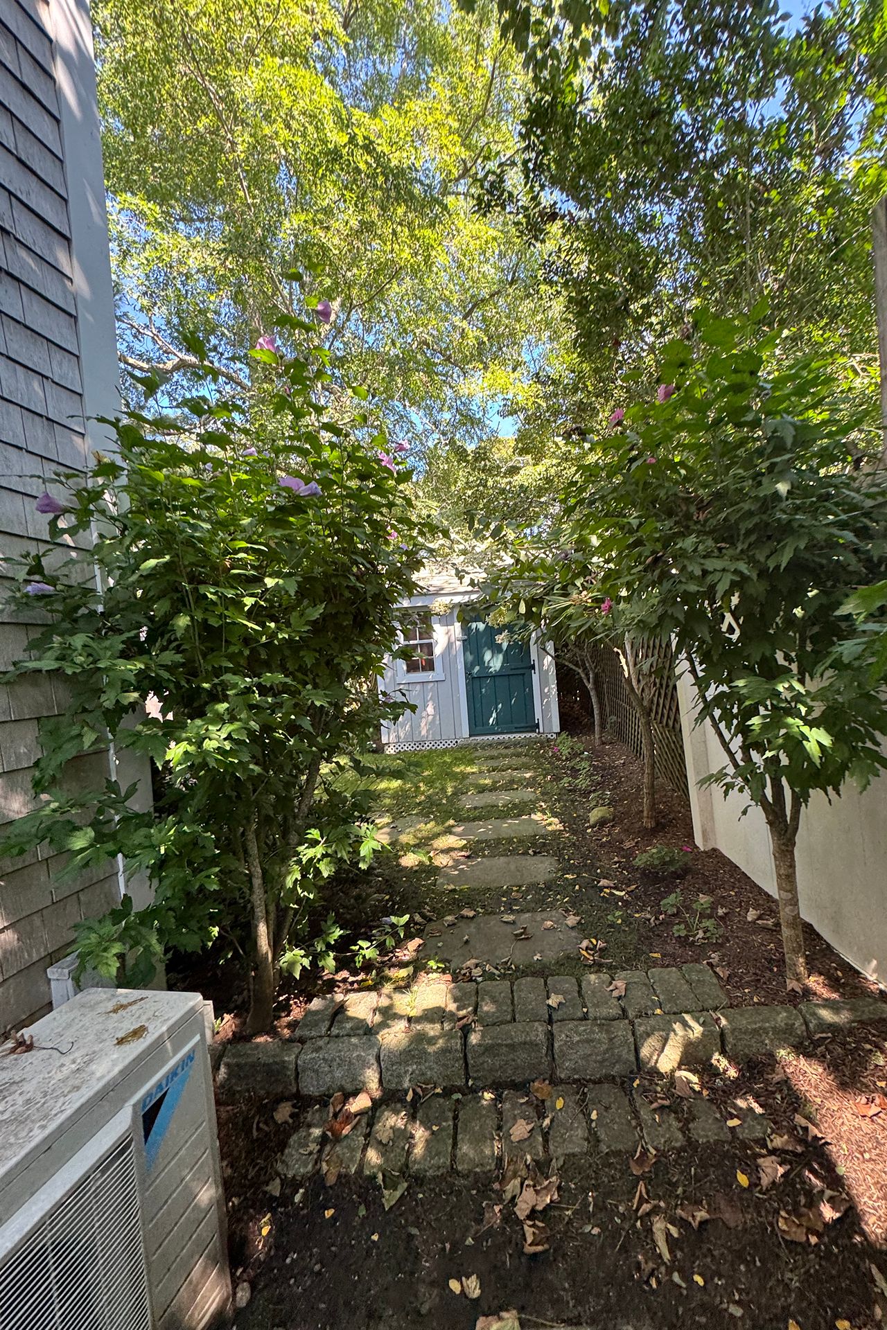 Stone path through a leafy side garden leads to a small outbuilding with a green door.