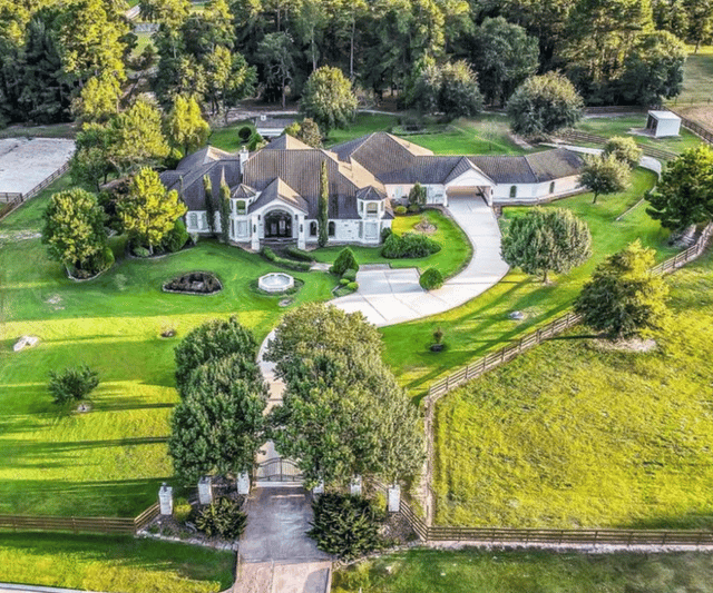 Aerial view of a large home with a curved driveway, landscaped lawn, and surrounding fields.