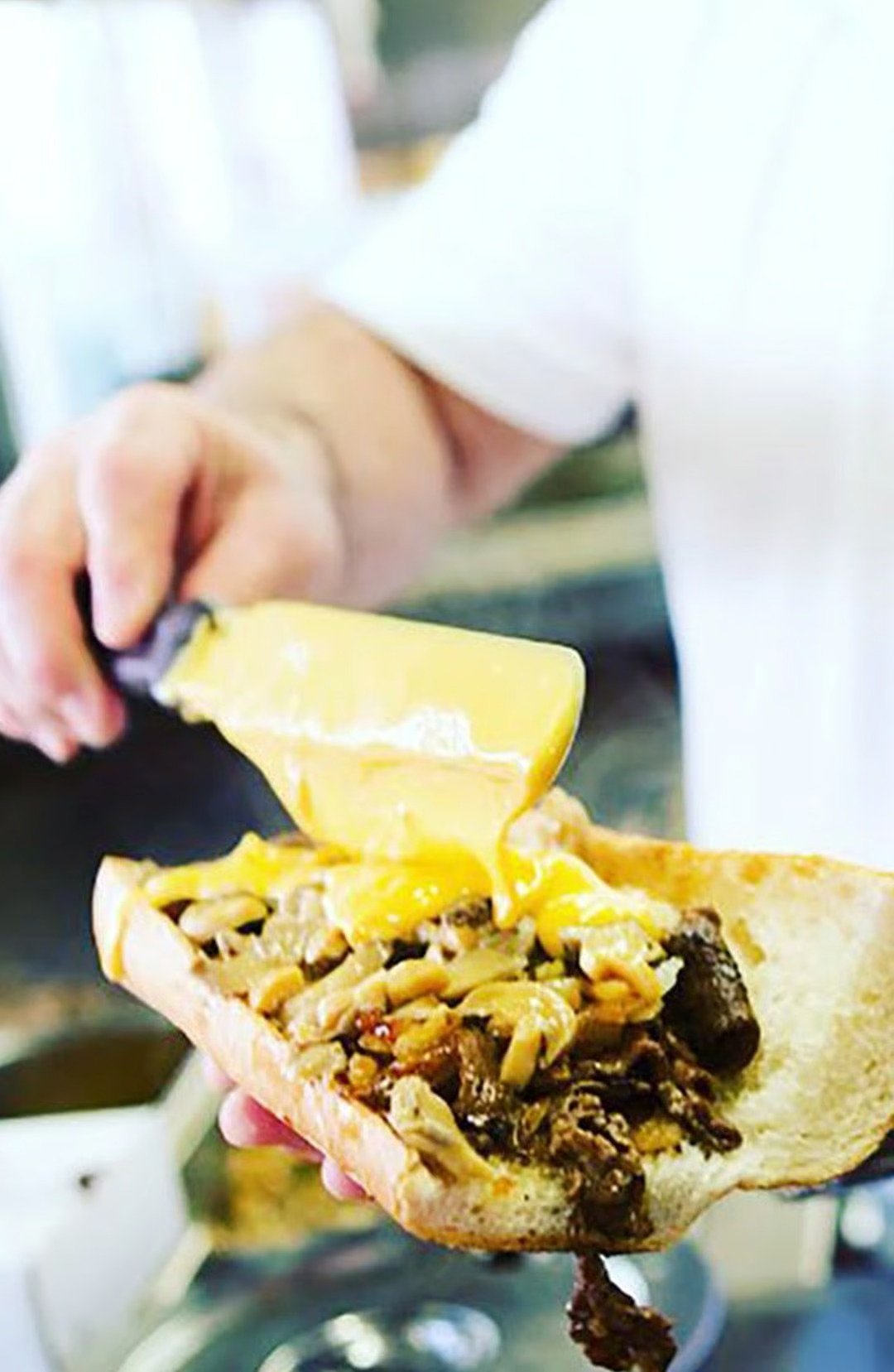 Melted cheese poured over a meat-and-onion sandwich on a roll.