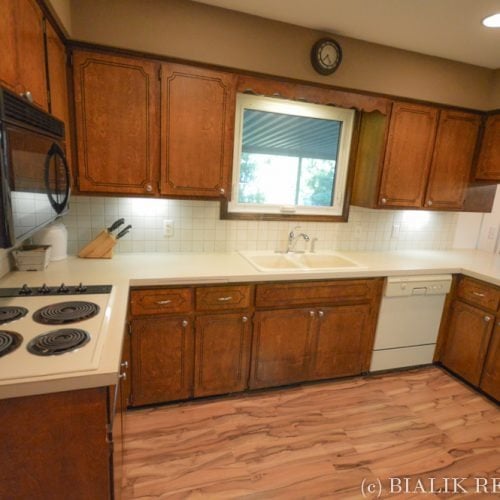Kitchen with reddish-brown cabinets, a window above the sink, and wood-look flooring.