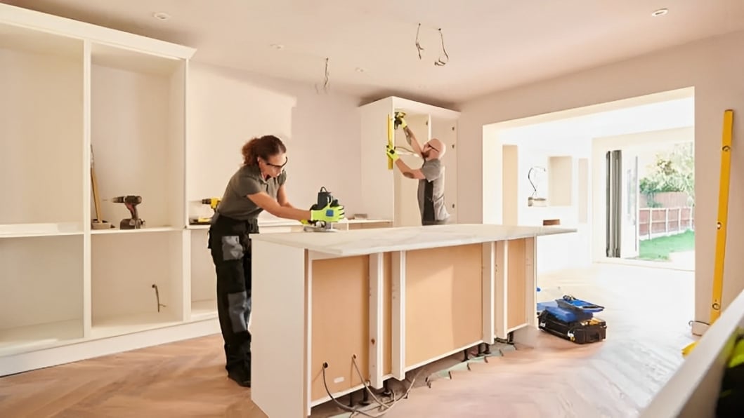 Kitchen under renovation with two workers installing cabinetry around a large island.