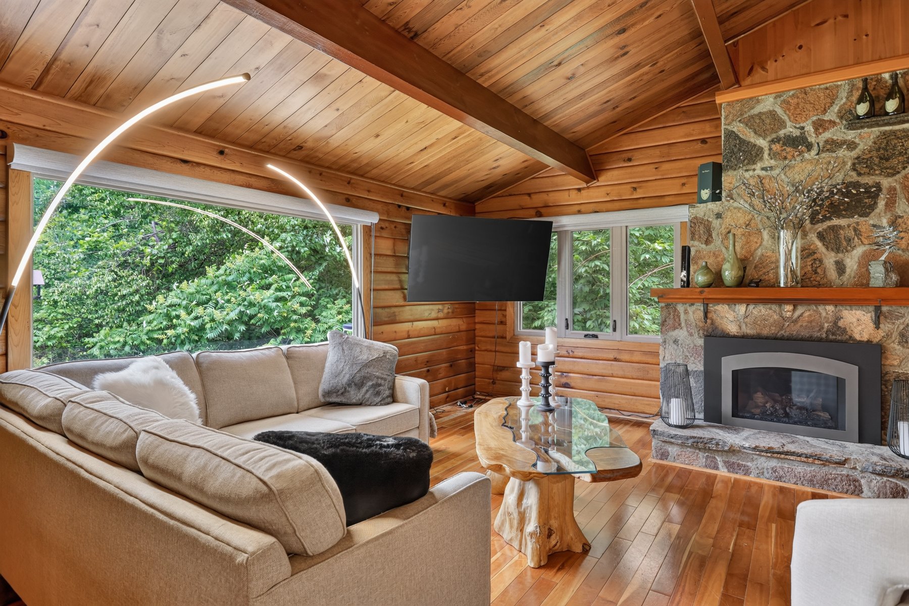 Living room with a vaulted wood ceiling, stone fireplace, and sectional beside broad windows.