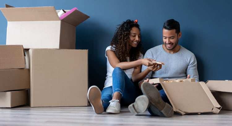 A smiling couple unpacks cardboard moving boxes together.
