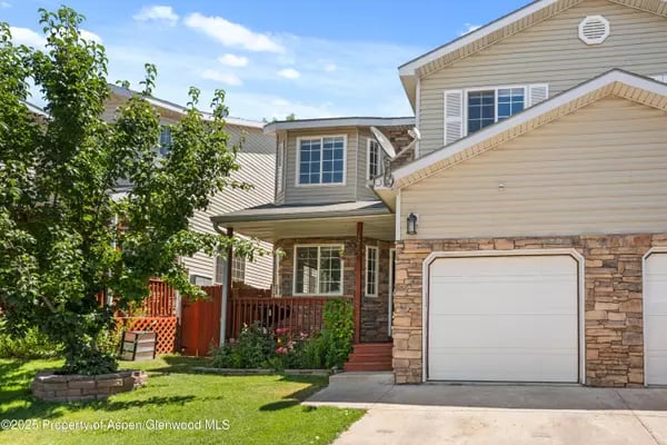 Beige multi-level home with stone accents, covered porch, attached garage, and green lawn.