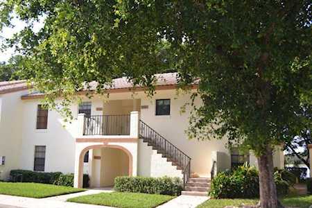 Two-story home with an exterior staircase, upper balcony, and arched entry beneath a large tree.