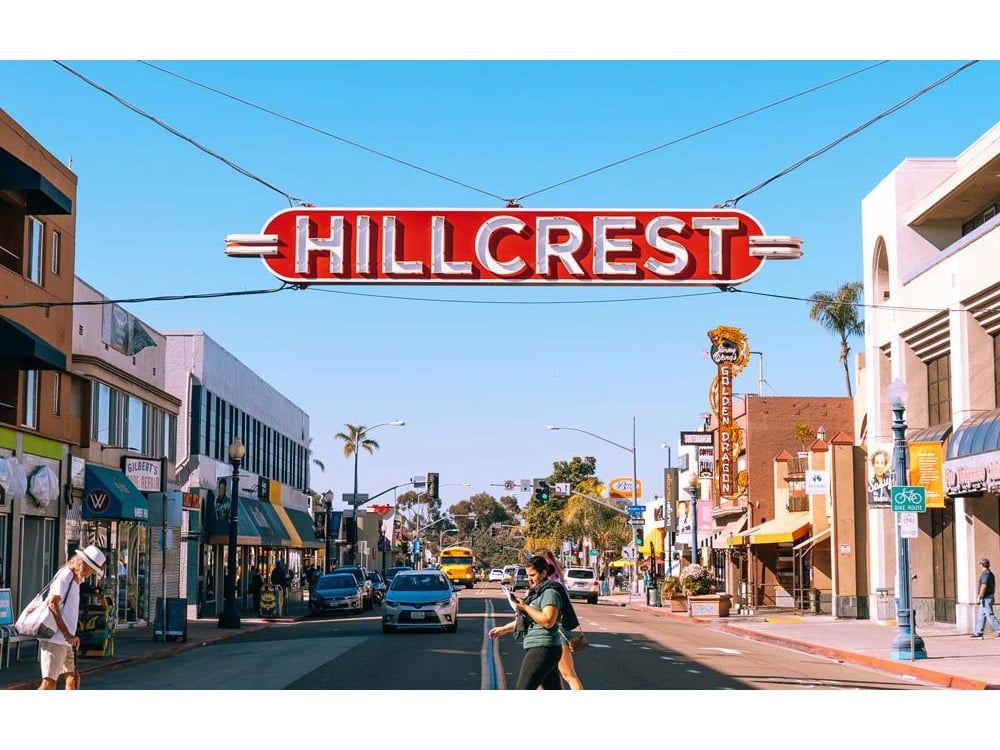 The iconic Hillcrest sign above a walkable street lined with shops and restaurants in San Diego, representing the vibrant lifestyle and central real estate appeal of the neighborhood.