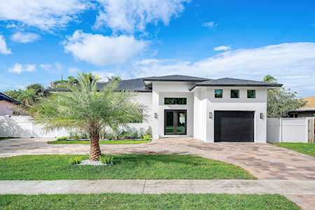 Contemporary white home with a black garage door, paver driveway, and palm tree on the lawn.